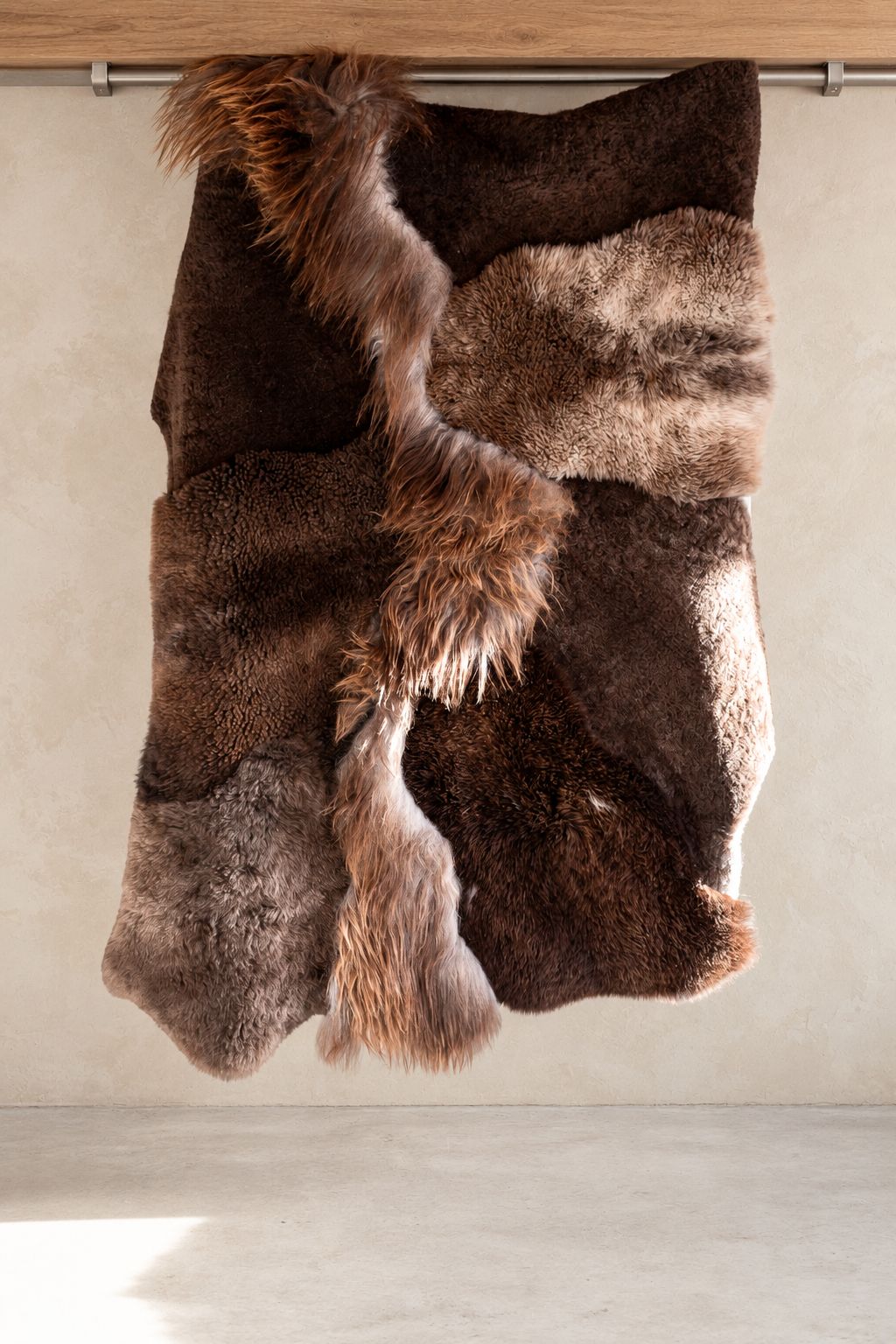 Tapis Mélangé brun chiné en peau de mouton naturelle présenté suspendu, vue complète du patchwork et des textures
